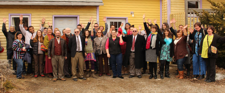 group of people waving in front of a yellow house