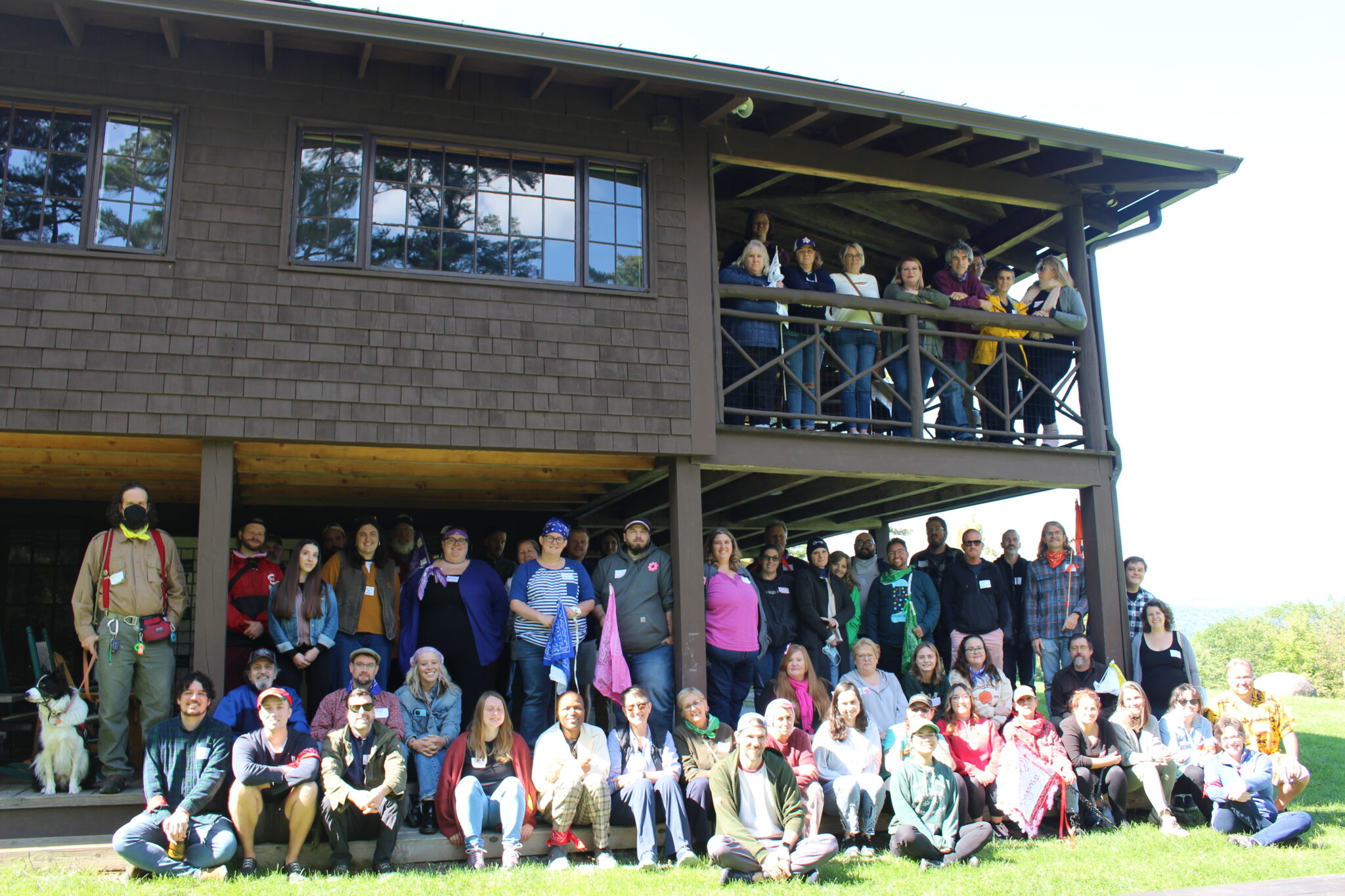 Photo of 63 staff members and one black and white dog outside of a building.