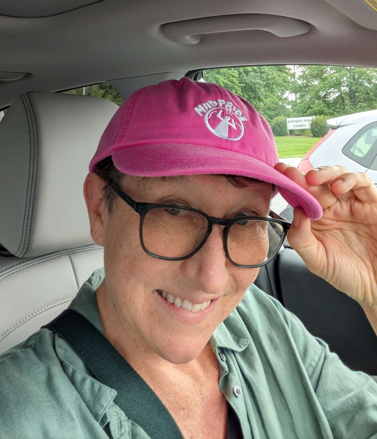 Selfie of a woman wearing glasses and a green shirt with a pink hat that says "Mad Pride"