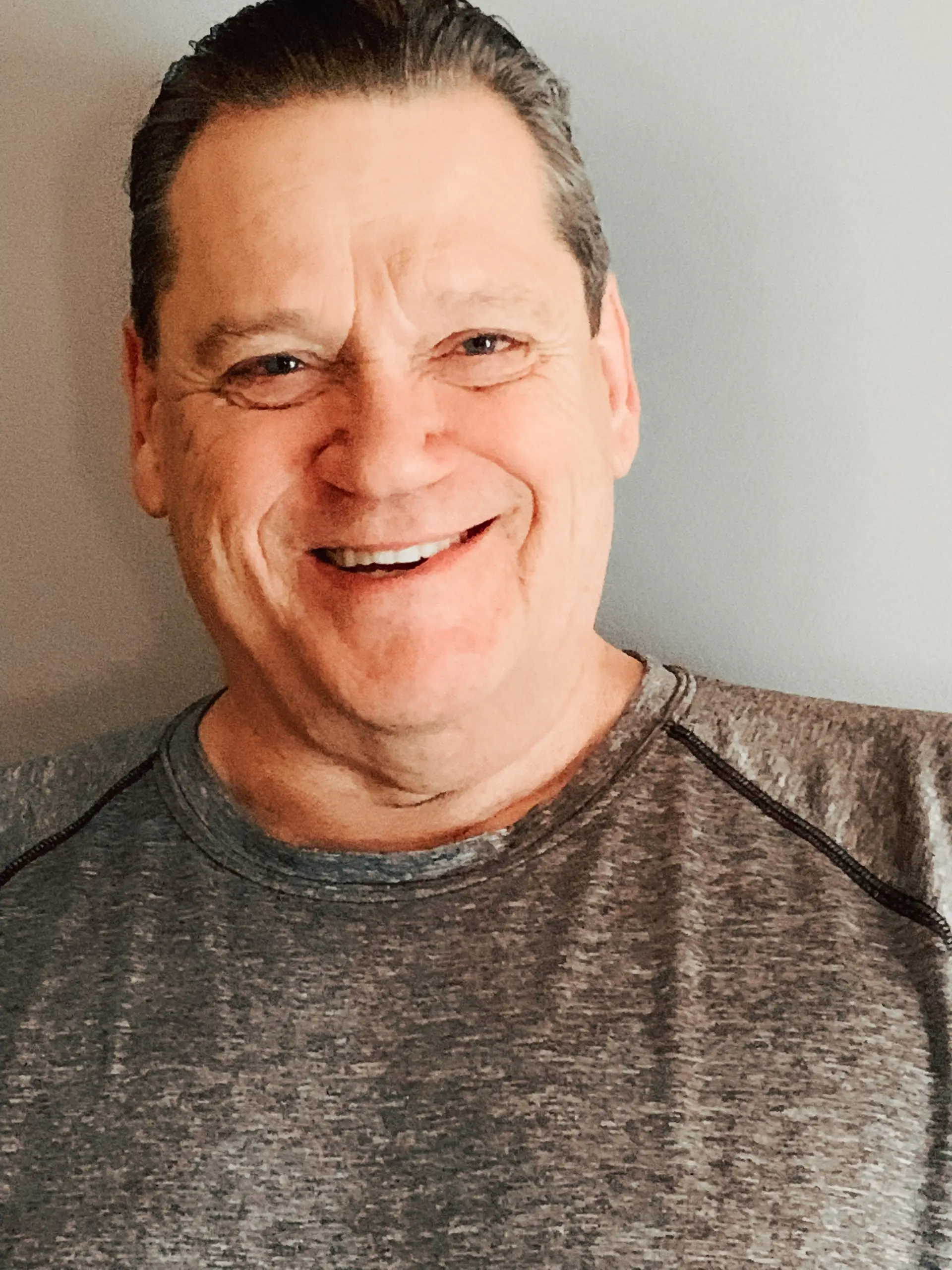 Photo of a man smiling wearing a gray shirt.