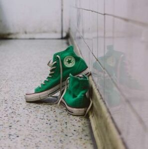 A pair of green converse on the ground with one shoe slightly on top of the other.