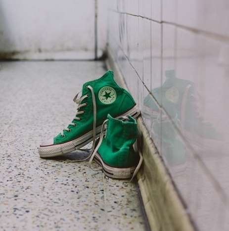 A pair of green converse on the ground with one shoe slightly on top of the other.