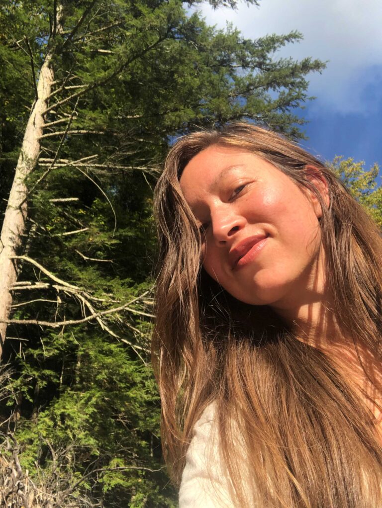 Selfie of a woman with long brown hair in front of a tree